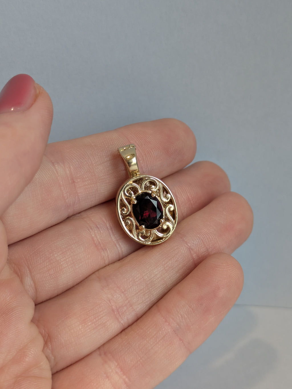 Gold pendant with a red gemstone held in a hand against a plain background