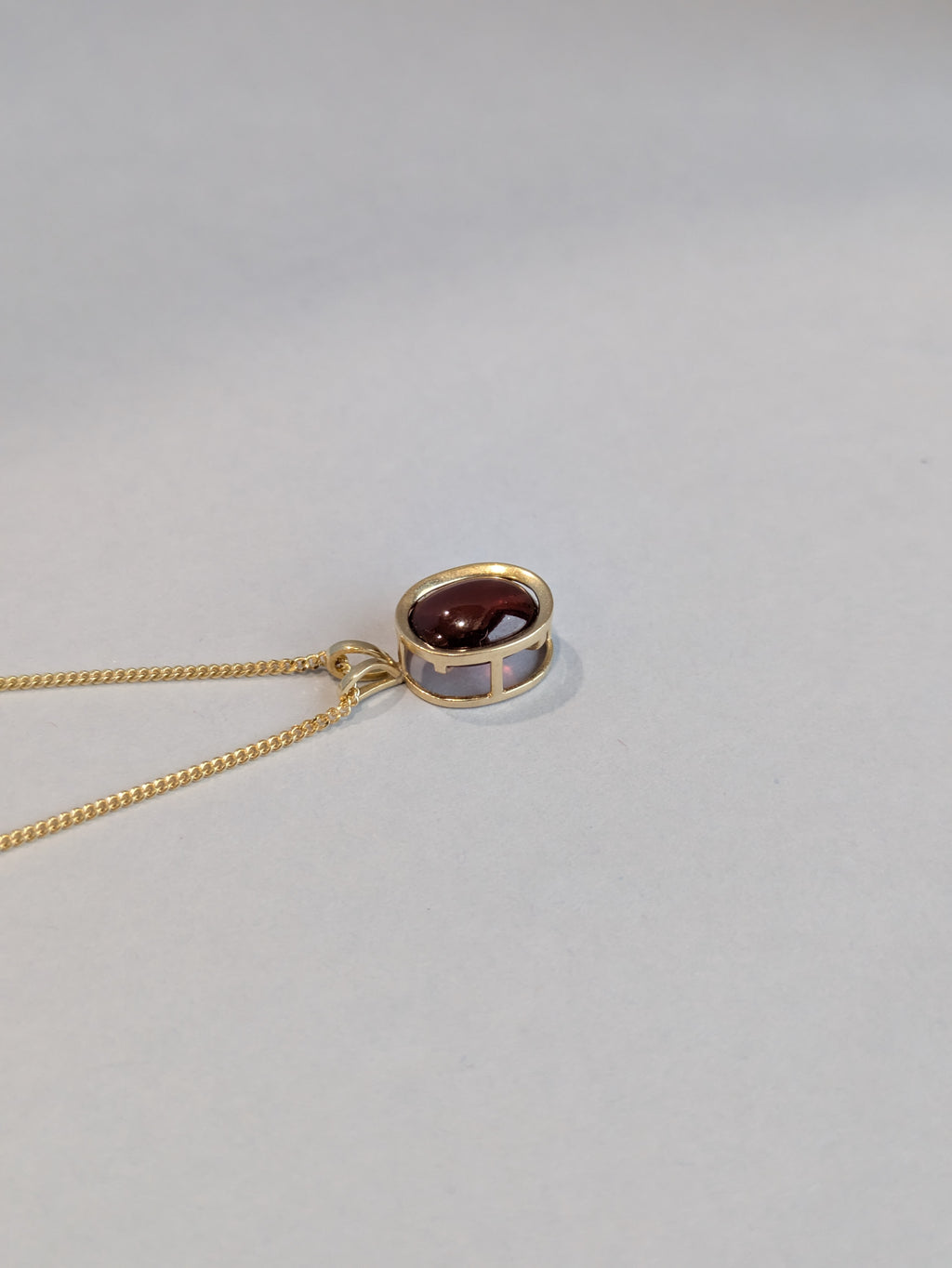 Gold necklace with a pendant featuring a red stone on a light gray background