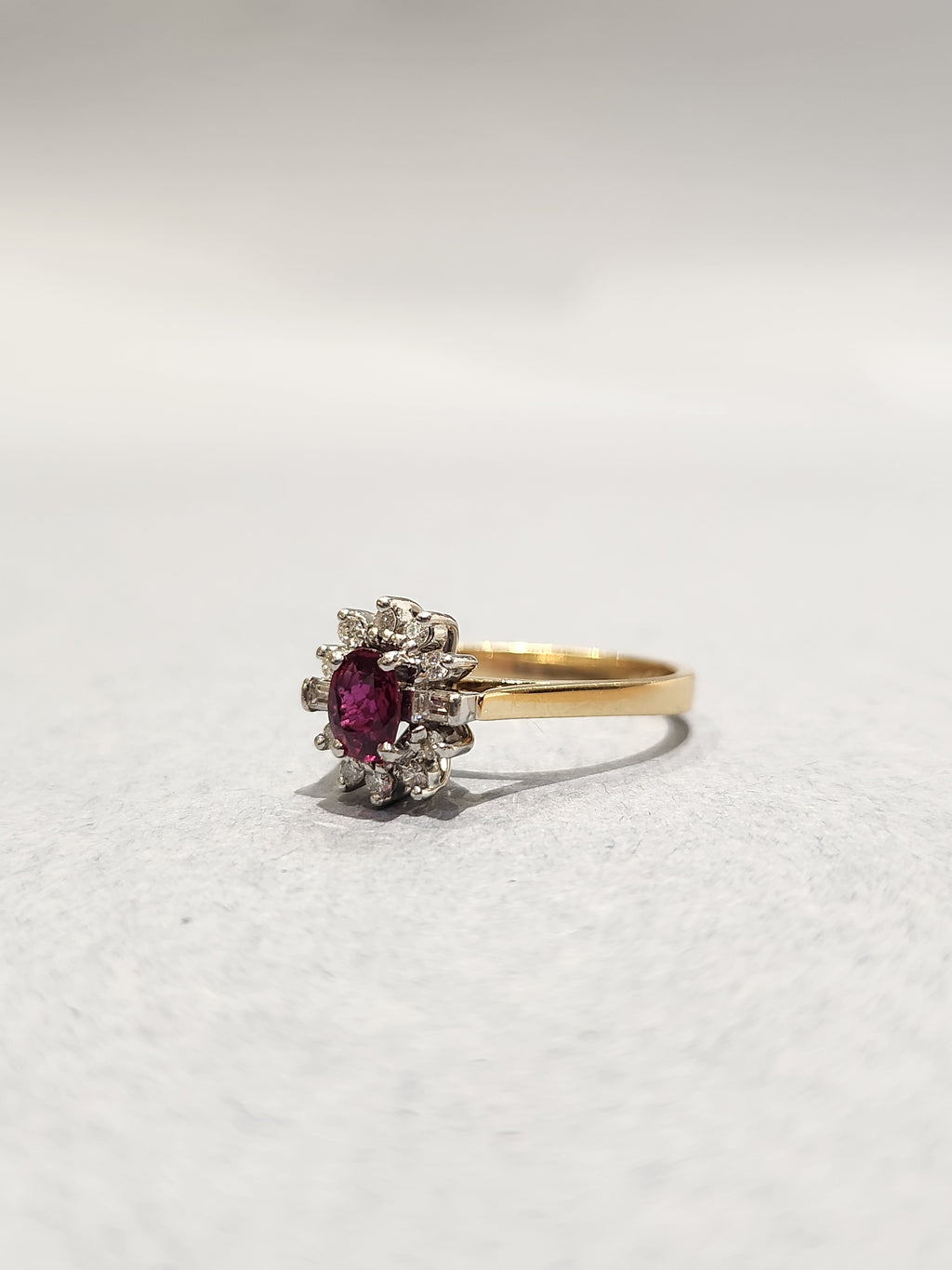 Gold ring with white gold settings holding a diamond halo and Ruby centre stone