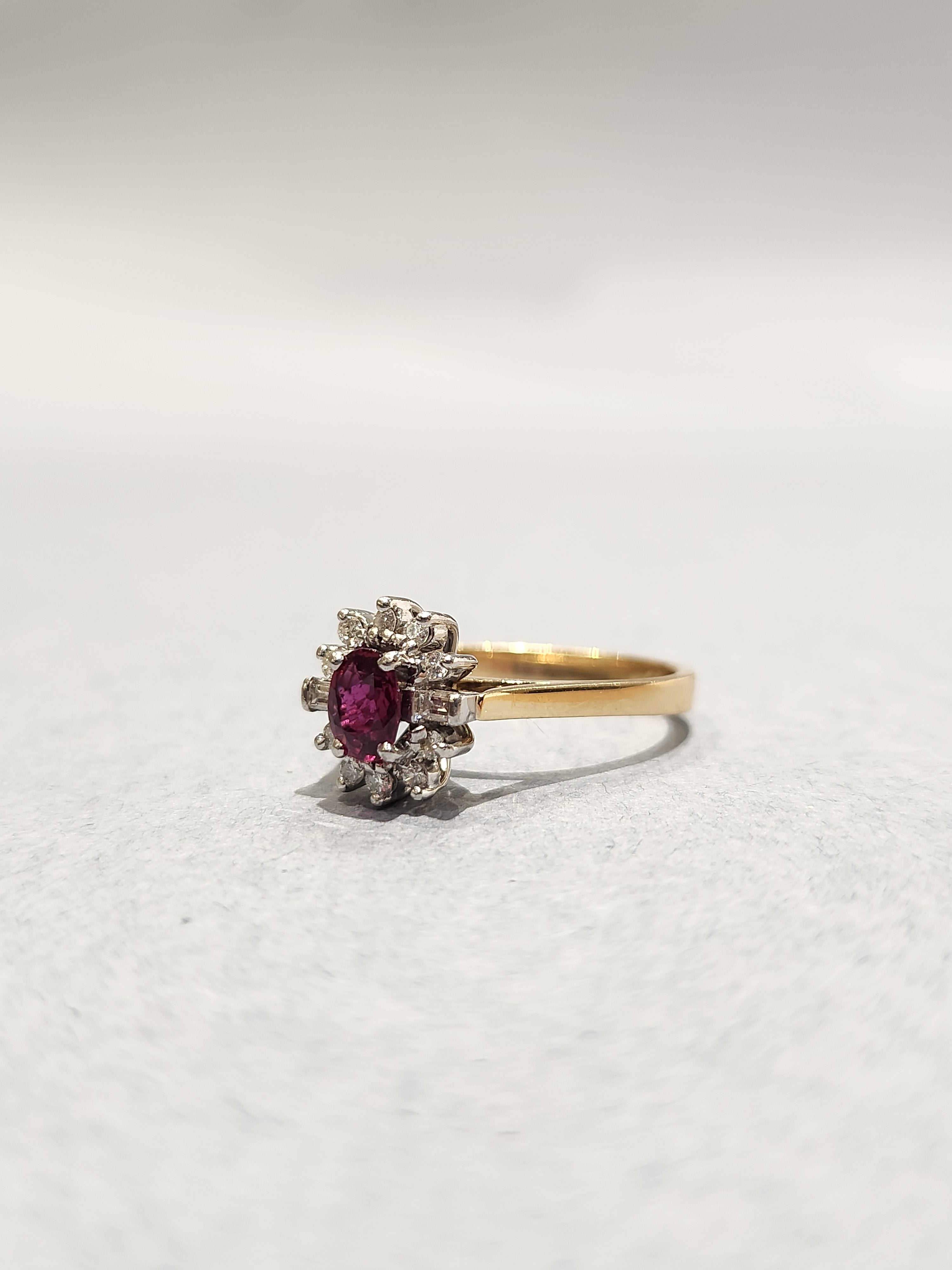 Gold ring with white gold settings holding a diamond halo and Ruby centre stone