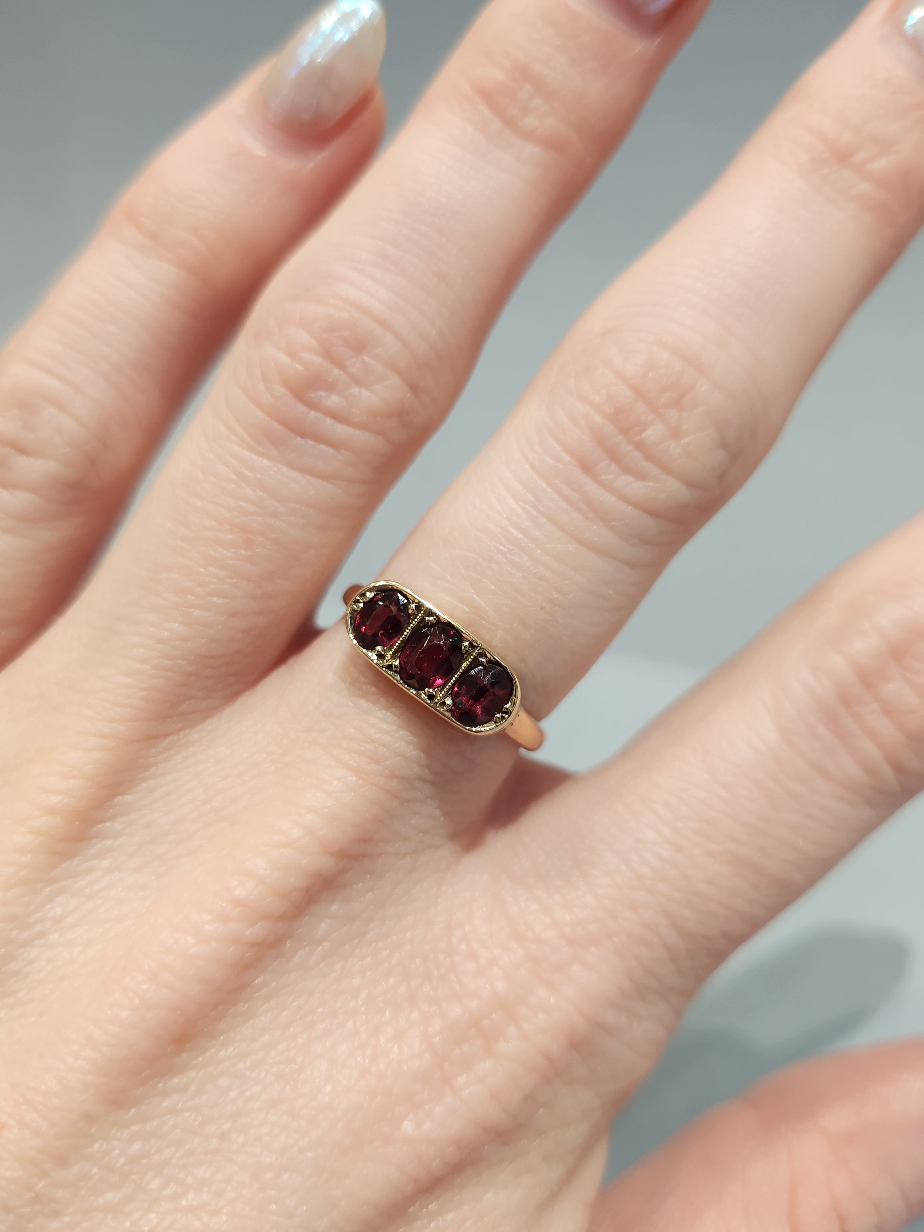 Trilogy ring, garnet oval cut with rose gold setting, worn on hand