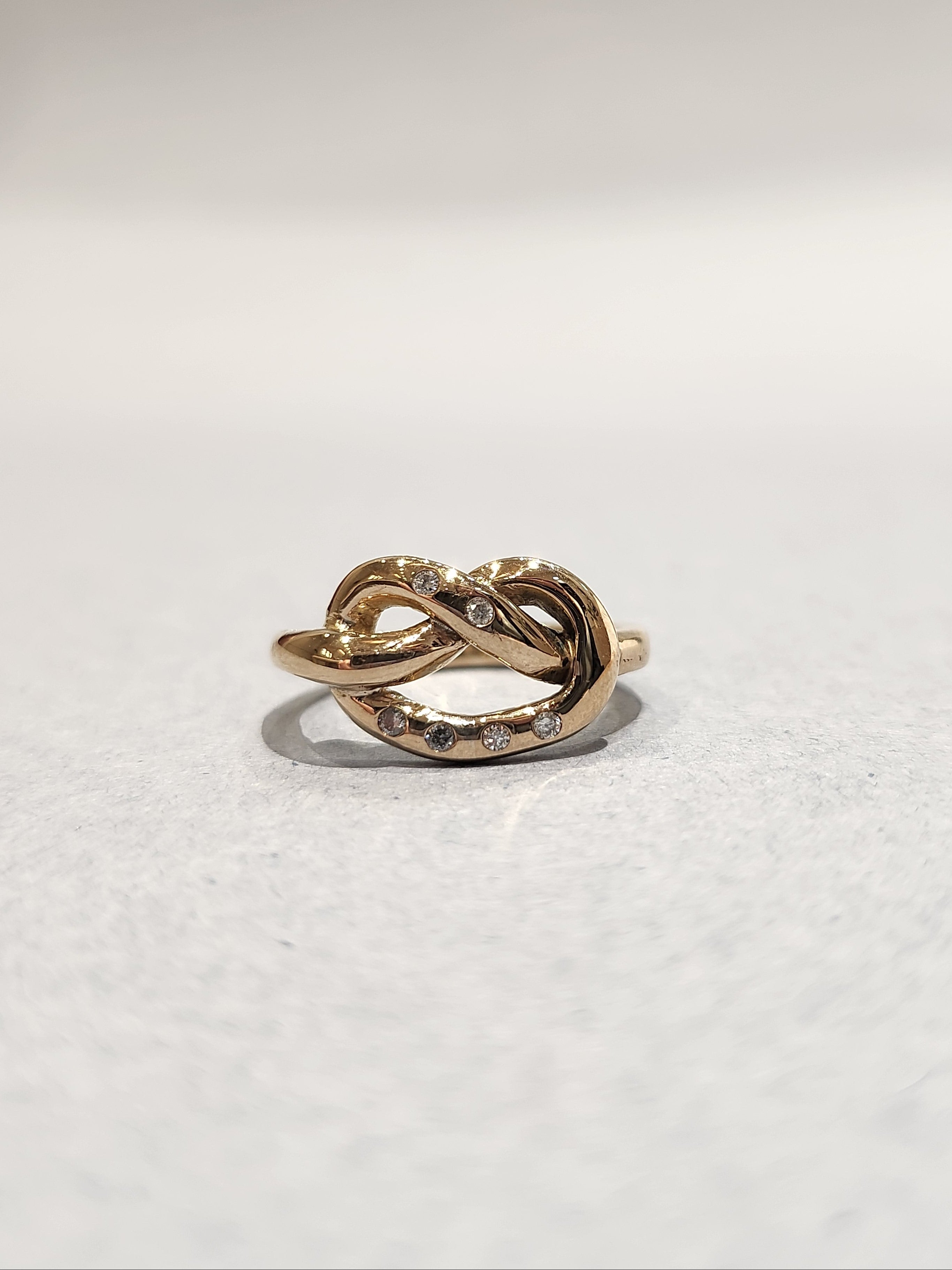 Gold ring in a knotted design, with 6
Round Diamonds flush set into the gold. 9ct Yellow gold. Pretzel ring. 
