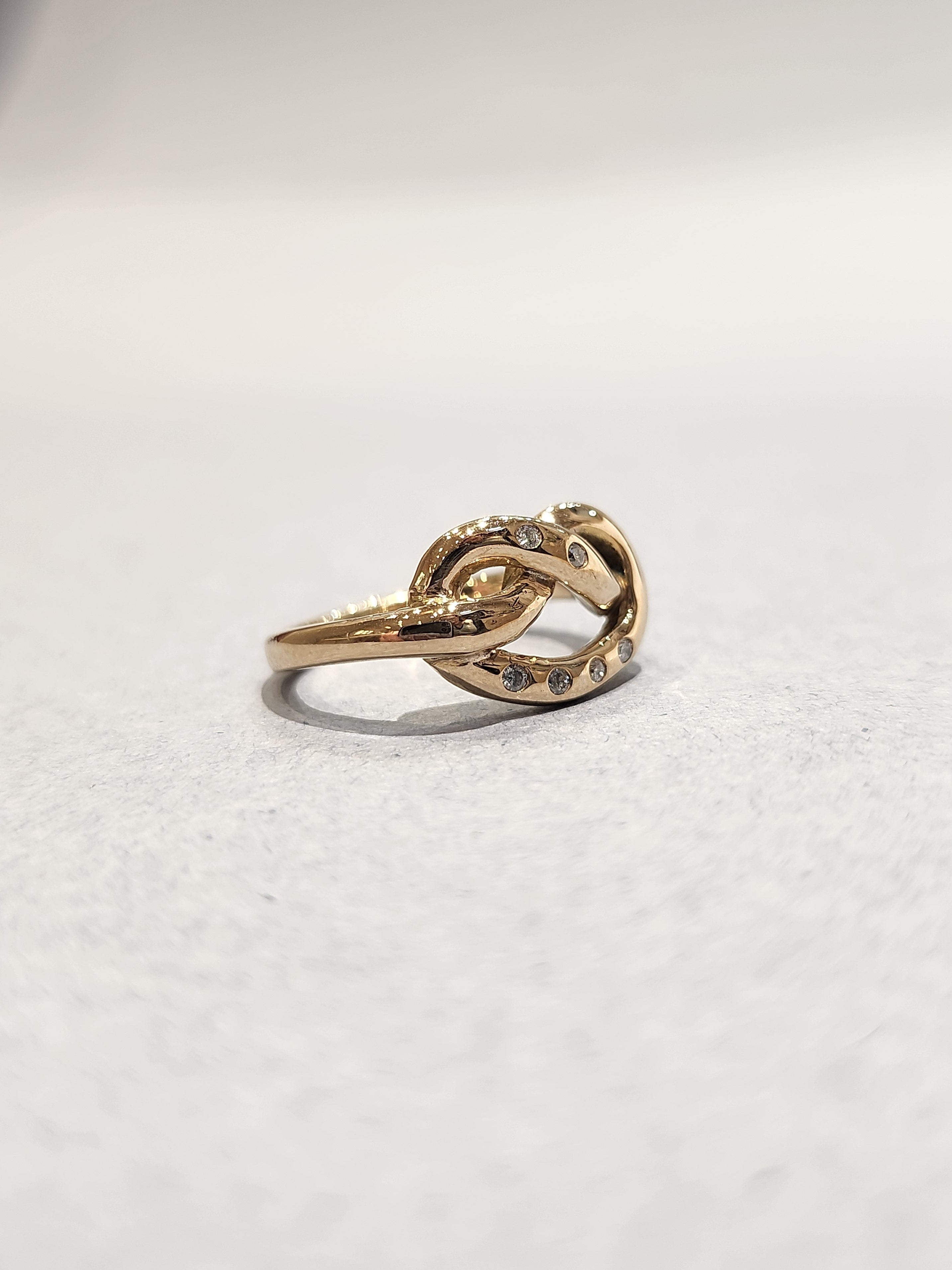 Side View of Gold ring in a knotted design, with 6
Round Diamonds flush set into the gold. 9ct Yellow gold. Pretzel ring. 