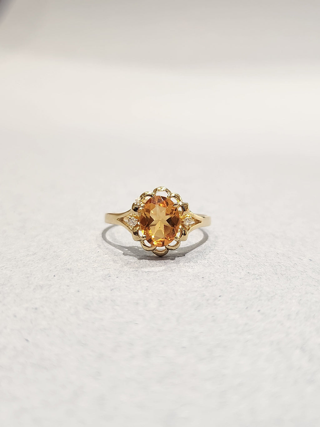 Front view shot of Gold ring with ornate gold work and large orange oval centre stone with 2 diamond side stones