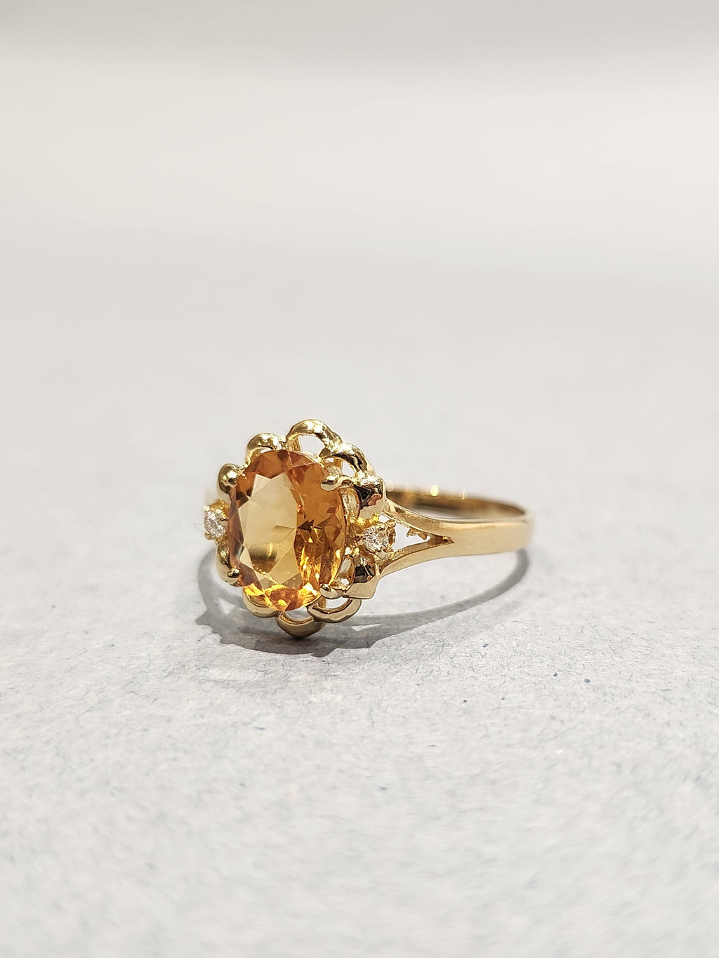 Off angle front view shot of Gold ring with ornate gold work and large orange oval centre stone with 2 diamond side stones