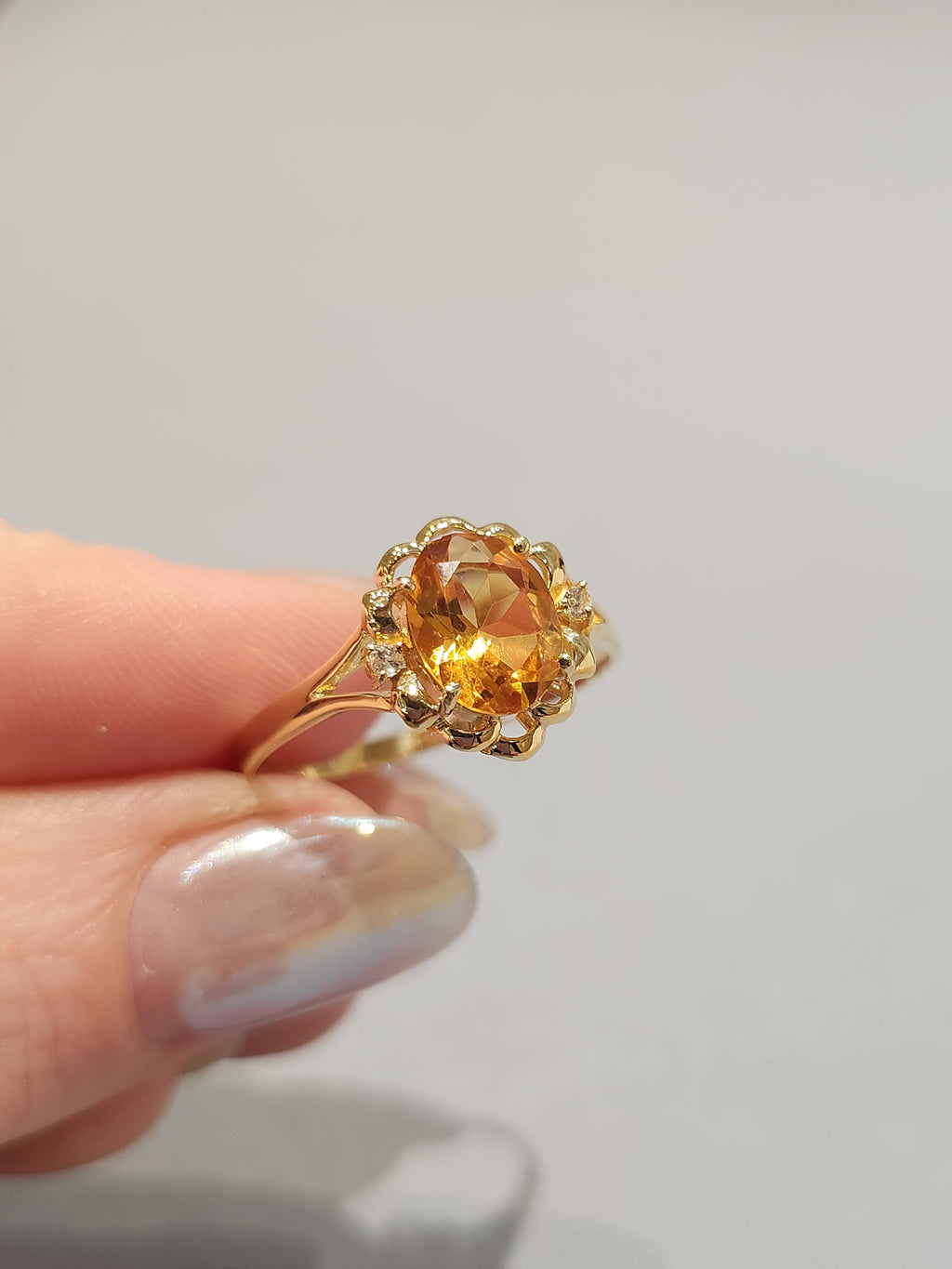 Off angle Front view shot of a hand holding the Gold ring with ornate gold work and large orange oval centre stone with 2 diamond side stones