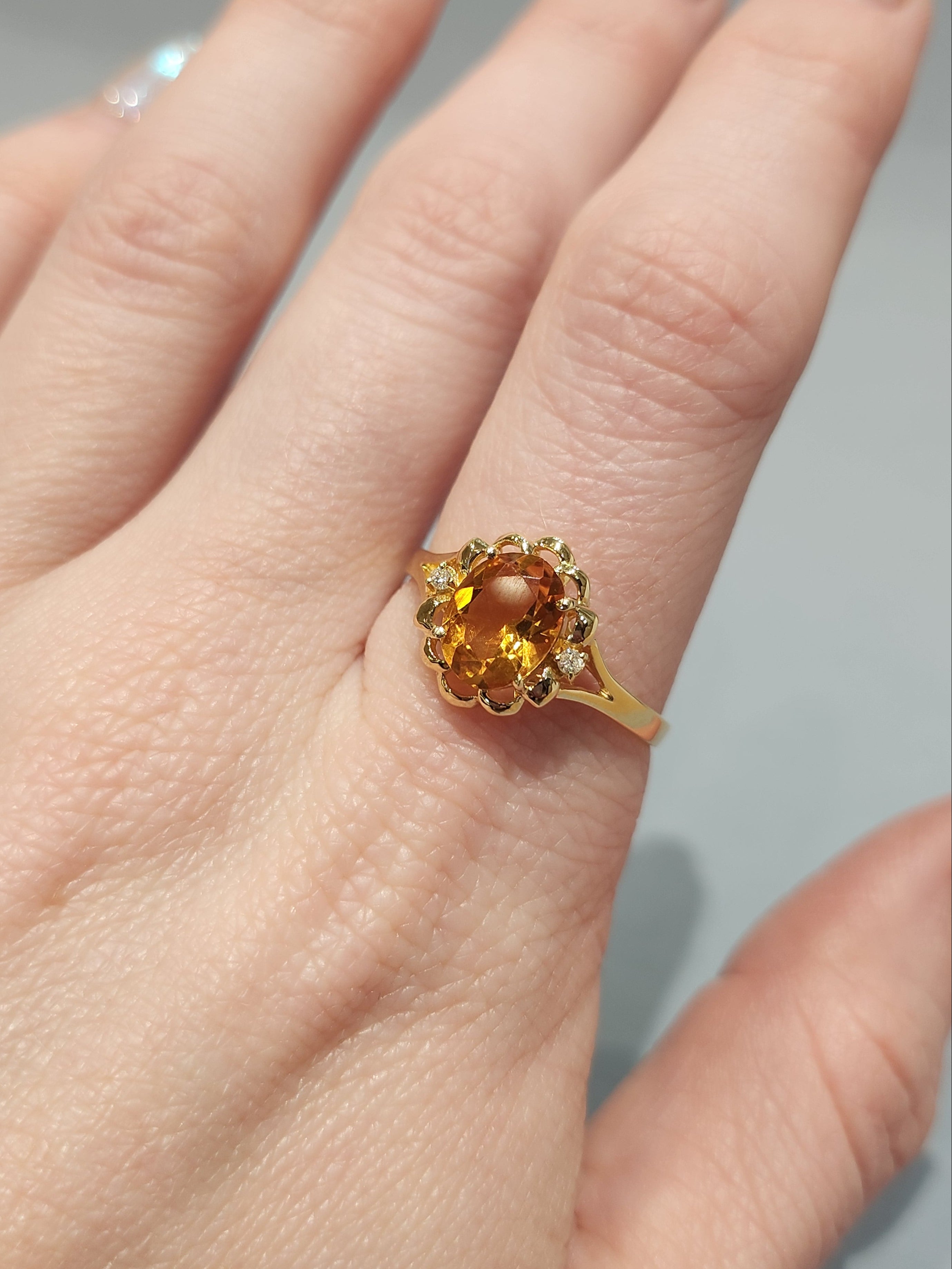 Front view shot of fair-skinned hand wearing the Gold ring with ornate gold work and large orange oval centre stone with 2 diamond side stones