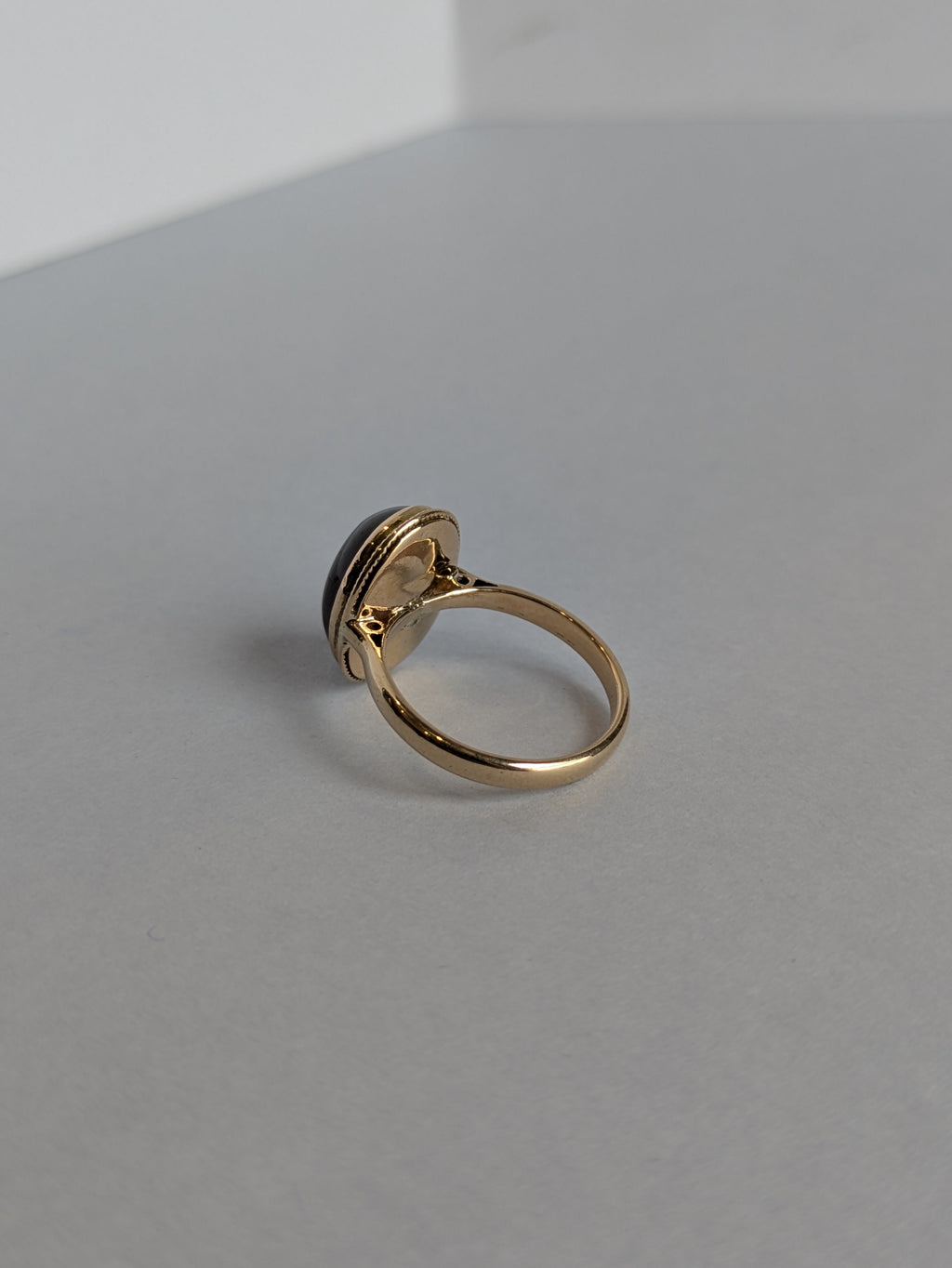 Rear view camera Shot of yellow gold ring set with deep red oval cabochon cut garnet bezel set, ring laying flat on white background showing underneath setting