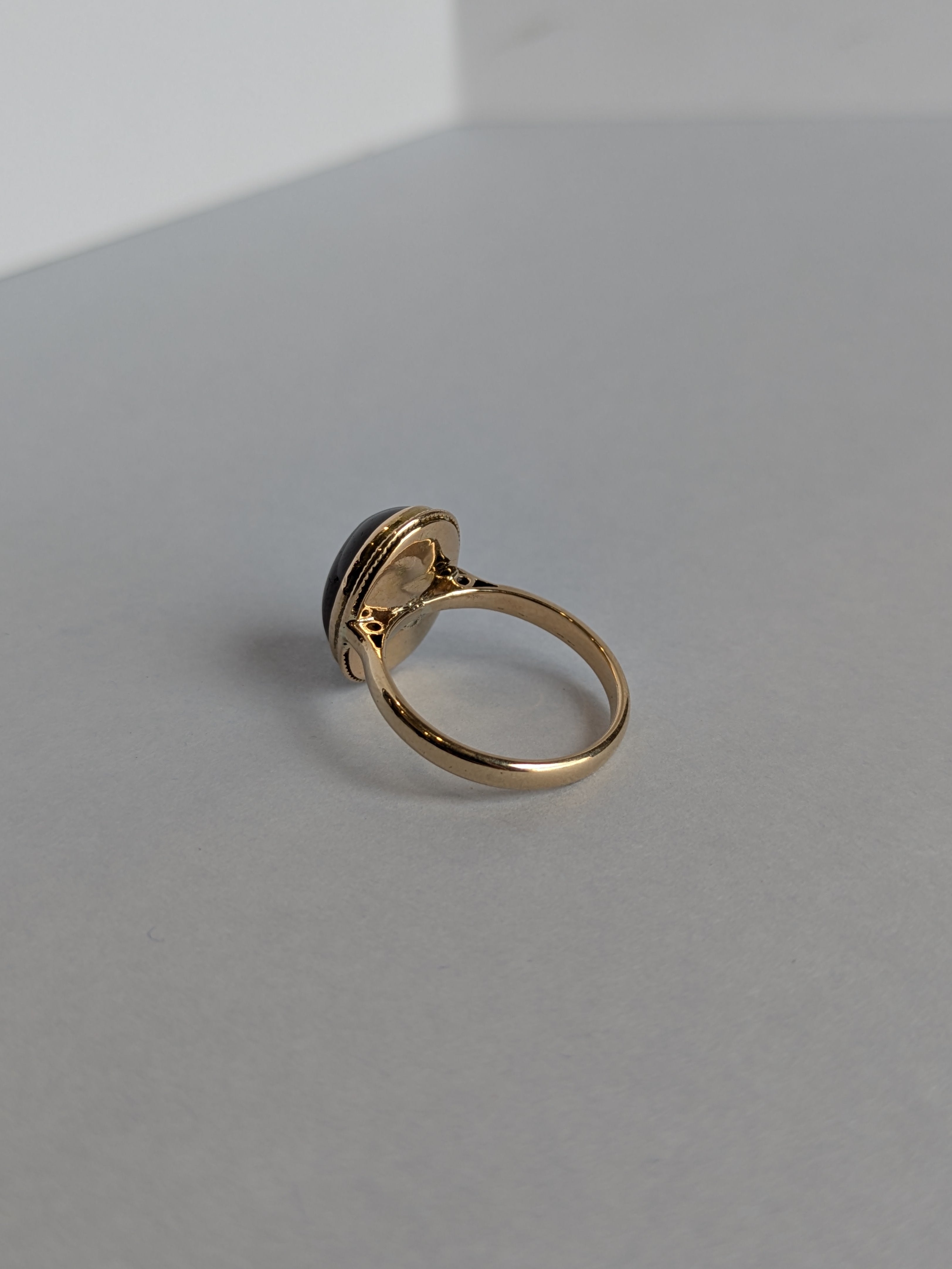 Rear view camera Shot of yellow gold ring set with deep red oval cabochon cut garnet bezel set, ring laying flat on white background showing underneath setting