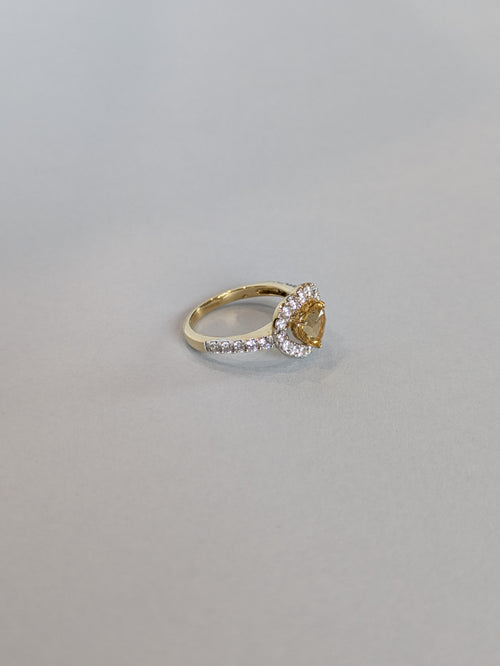 Slight off Angle Front on Shot of yellow gold ring set with heart shaped citrine with a halo, ring laying flat on white background showing stones set on shoulder