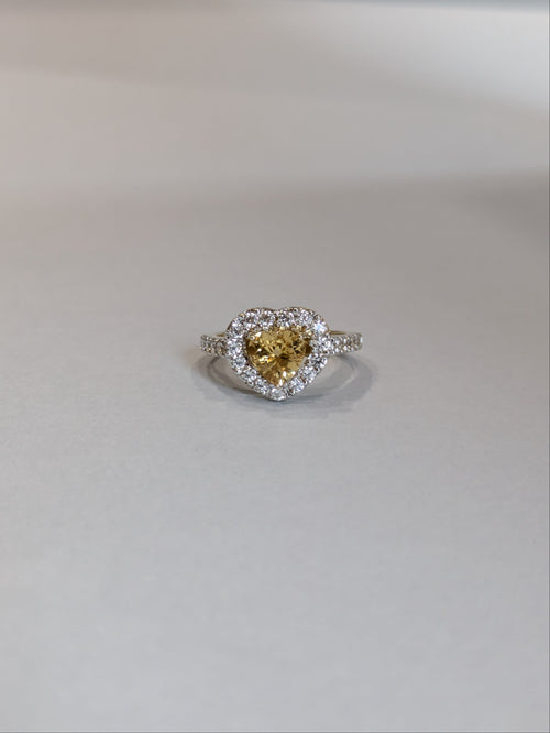 Front on Shot of yellow gold ring set with heart shaped citrine with a halo, ring laying flat on white background