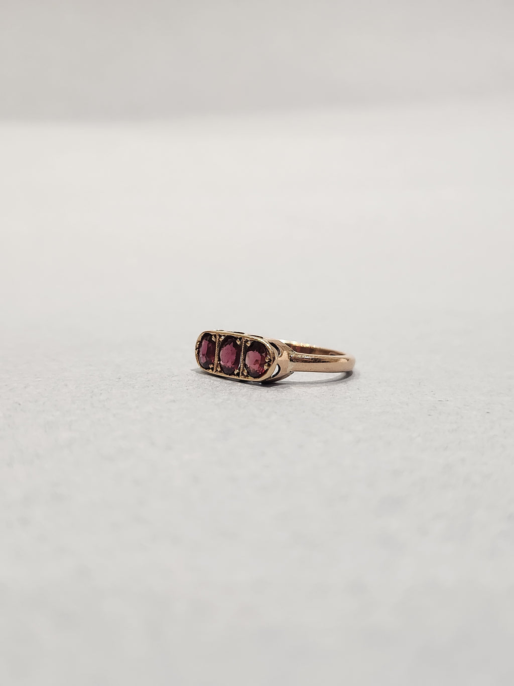 Slight off angle Front view shot of rose gold trilogy ring set with three oval cut garnets bead set laying flat on white background