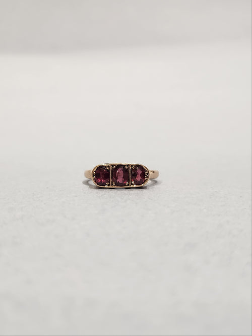 Front view shot of rose gold trilogy ring set with three oval cut garnets bead set laying flat on white background